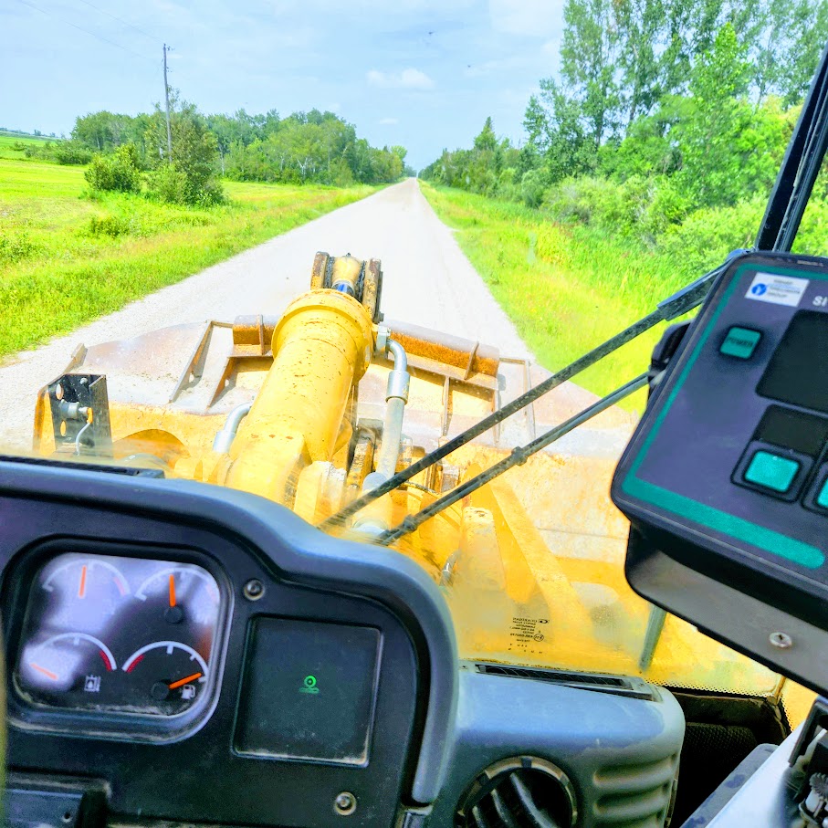 Grader cab view on a summer prairie road